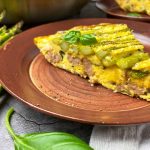 Horizontal close-up image of a wedge of vegetable and meat frittata on a brown plate.