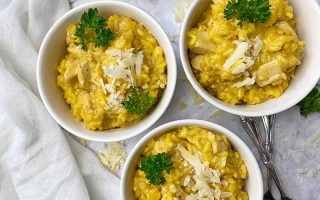 Horizontal top-down image of three white bowls filled with a thick and creamy yellow stew topped with herbs and shredded parmesan.