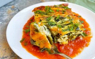 Horizontal image of a slice of an egg bake over a base of tomato sauce on a white plate.