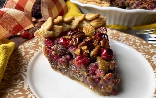 Horizontal image of a slice of a fruit and nut pastry on a white plate next to plaid fabric and a casserole dish.