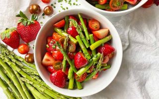Horizontal image of two white bowls filled with a mix of green vegetables, strawberries, and tomatoes.
