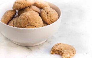 Horizontal image of a bowlful of sugar-coated cookies, with one on the marble counter with a bite taken out of it.