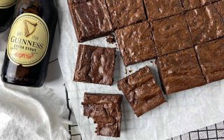 Horizontal image of portioned individual square baked goods on a parchment paper next to bottles of beer.