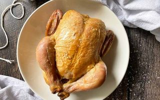 Horizontal image of a whole cooked poultry on a cutting board next to twine and towels.