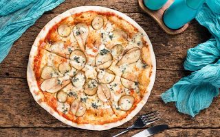 Horizontal image of sliced pears and cheese on a round flatbread next to a blue napkin.