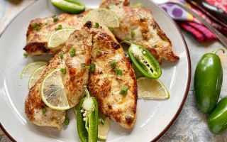 Horizontal image of a white plate with seared pieces of meat garnished with lime wedges and pepper halves.