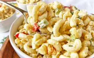 Horizontal close-up image of a spoonful of a chilled and creamy elbow macaroni dish in a white bowl with assorted vegetables.