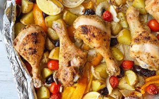 Horizontal image of cooked drumsticks on top of assorted vegetables on a foil-lined plate.