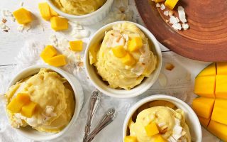 Horizontal top-down image of small white bowls filled with scoops of an orange-colored frozen dessert topped with various garnishes next to a brown plate.