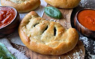 Horizontal image of small half-moon savory pastries on a wooden board next to herbs and tomato sauce.