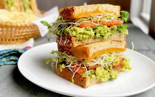 Horizontal image of a stacked vegetarian sandwich on a white plate on a wooden table.