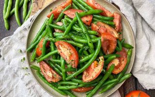 Horizontal top-down image of vibrant assorted vegetables mixed with herbs on a brown plate on top of tan towels.