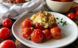 Horizontal image of two plates with a savory vegetable casserole next to fresh vegetables, herbs, and a white towel.