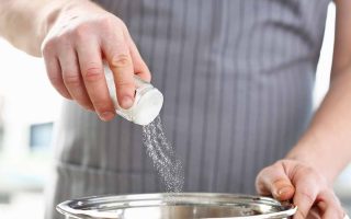 Horizontal image of a chef wearing an apron seasoning food in a pot.