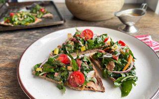 Horizontal image of triangles of bread topped with greens and sliced tomatoes on a white plate.